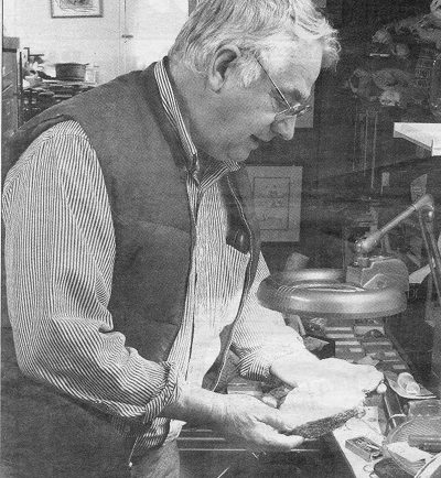 Graham Beard standing in his home, looking at a fossil under lamplight. c. 1995