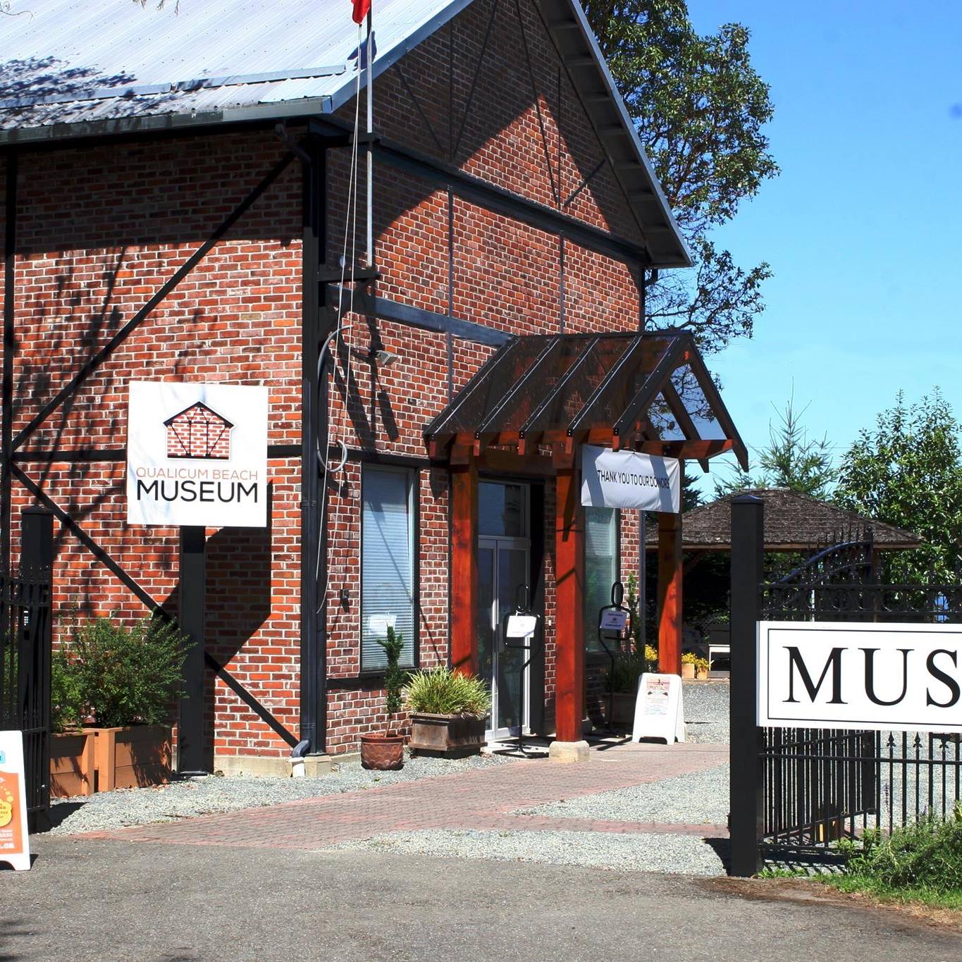 A two-storey building built of red bricks and black metal beams, photographed on a sunny day.