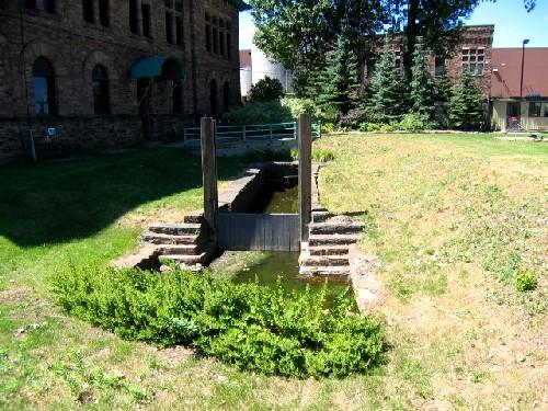 Green grass and shrubs in front of a canoe lock, General Office Building and Machine Shop in background.