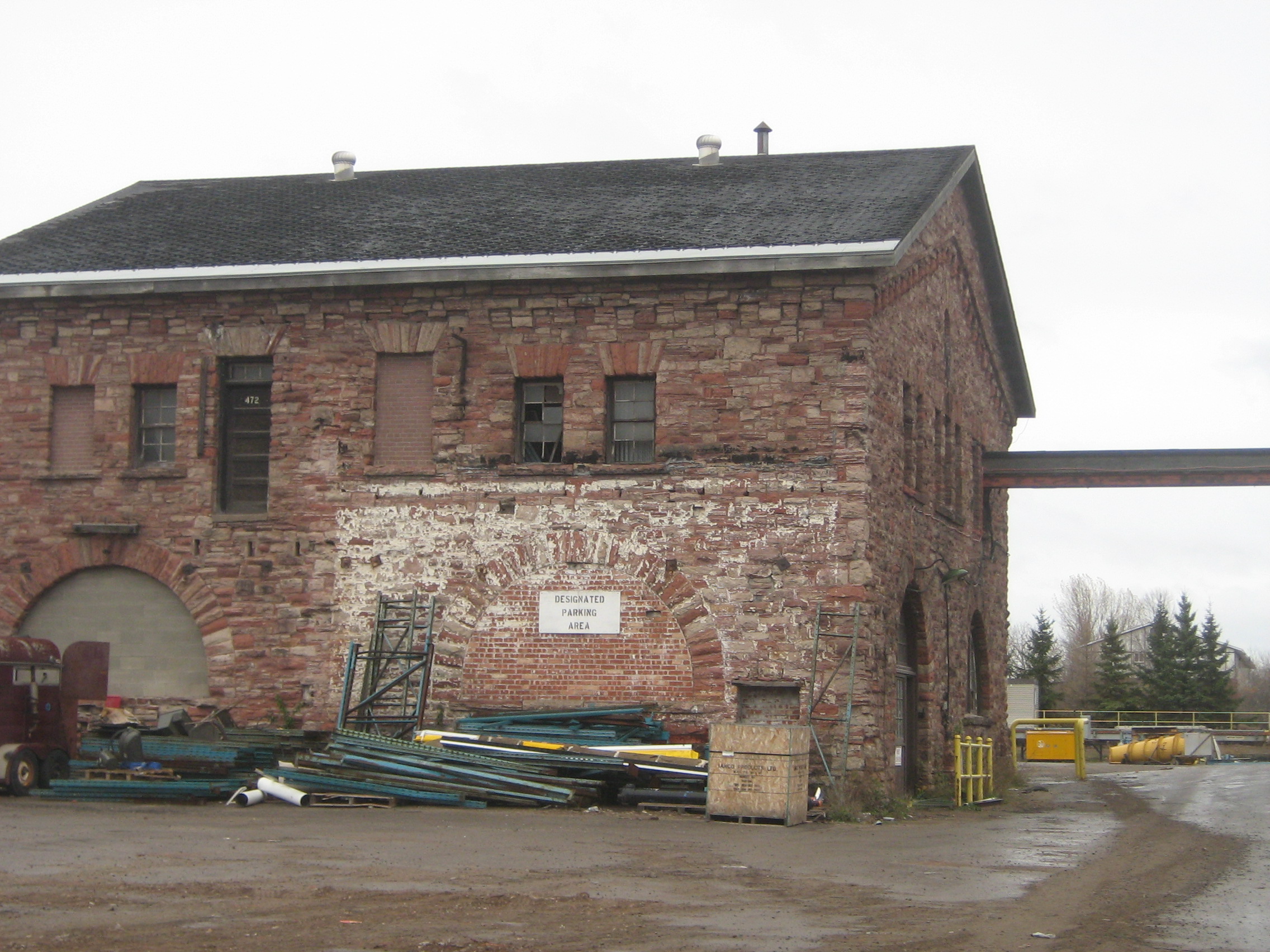 Sandstone building photographed on a grey day. Green steel pipes piled in front of the building.