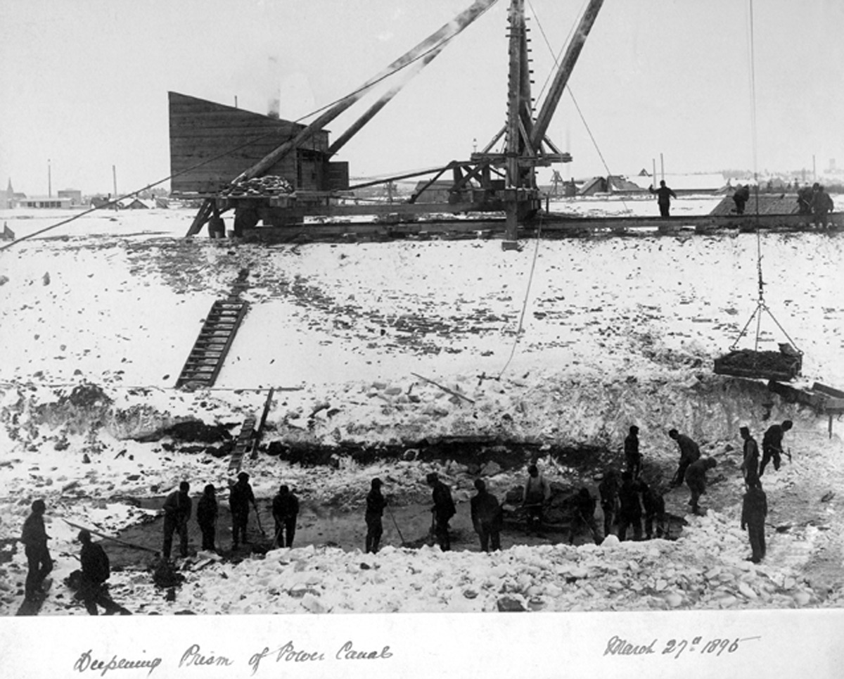 Men are seen digging a deep hole in the construction of the power canal. Snow on the ground.