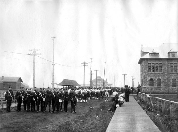 Soldiers standing to the left of the administrative building on a wooden sidewalk.