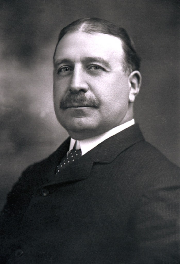 Black and white portrait of Francis Clergue. He wears a black suit and tie, has a moustache and his dark hair is parted in the middle.