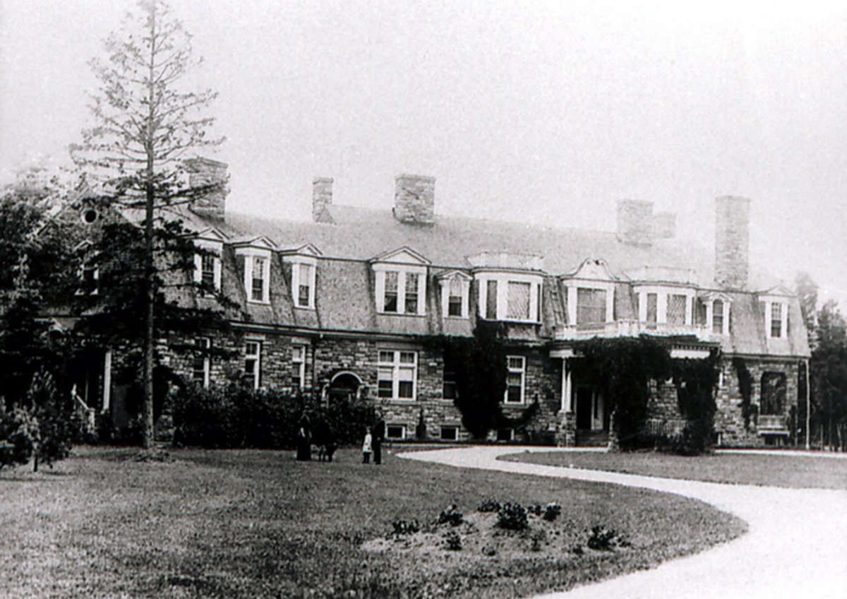 Path leading up to stone mansion. People standing in front of the mansion on lawn.