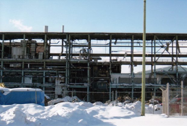 The bare beams of one of the modern buildings are exposed through demolition. There is snow in the foreground of the image. The building looks decrepit.
