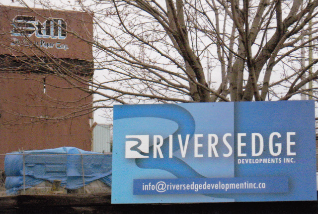 Photograph of the Riversedge Developments Inc. sign mounted on the fence of the St. Mary's Paper Corp. property.