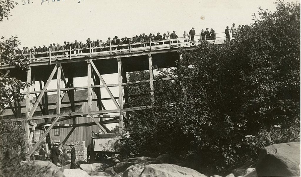 A crowd on a bridge watches a load of drink dropped down from the bridge