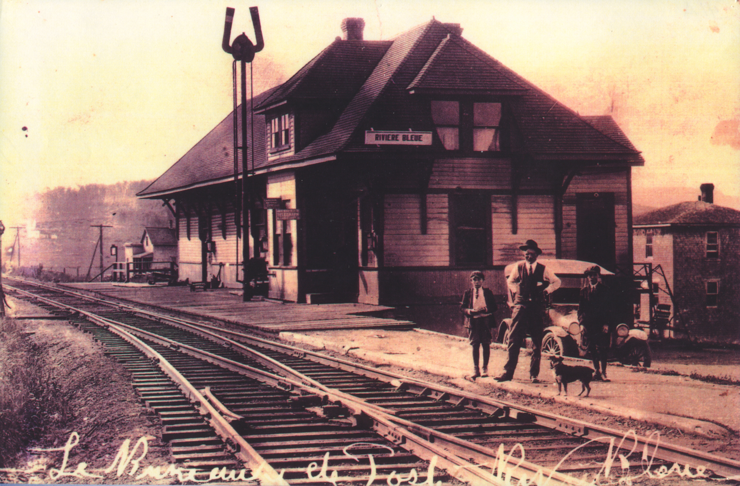 Un homme et deux garçons devant la gare de Rivière-Bleue