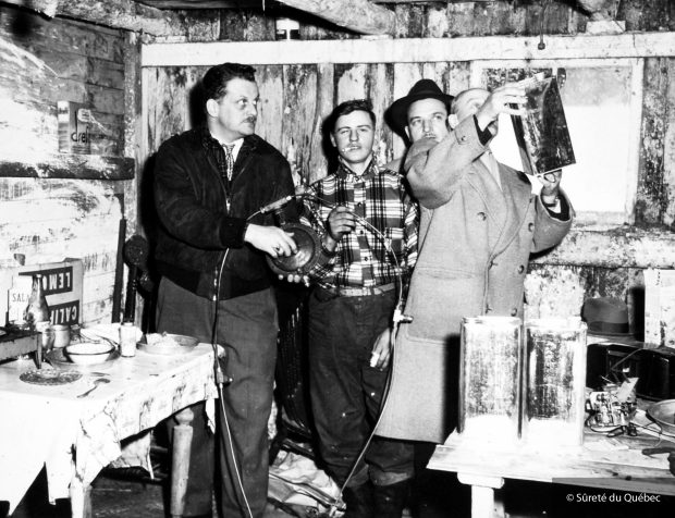 Two liquor policemen including Roch L'Écuyer on the left examine an illegal still during a raid