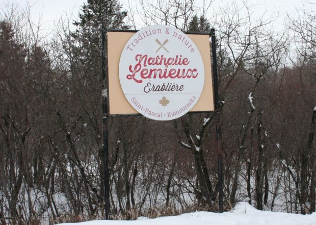 Beige sign with brown border and central white ellipse bearing the inscription. Tradition & nature in the arch above. The name Nathalie Lemieux appears in red cursive letters above Érablière.” Bottom: Saint-Pascal • Kamouraska and maple leaf. Snowy winter environment, bare trees.