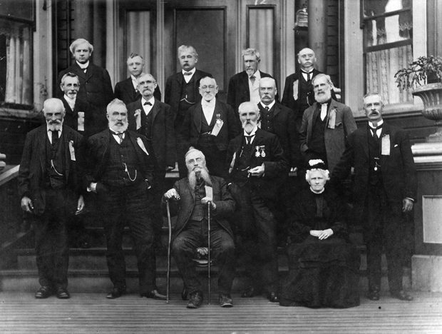 A black and white group photograph of one woman and 15 men formally dressed and organized into three rows. The bottom row includes an elderly Philip Jackman who stands on the left. The first row also includes three men standing and one man and one woman seated. The back two rows consist of five men each standing on steps.
