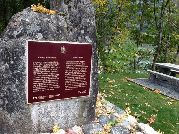 A photograph of a burgundy coloured plaque placed on a large granite stone at Yale, British Columbia. The plaque highlights the history of the construction of the Cariboo Wagon Road.
