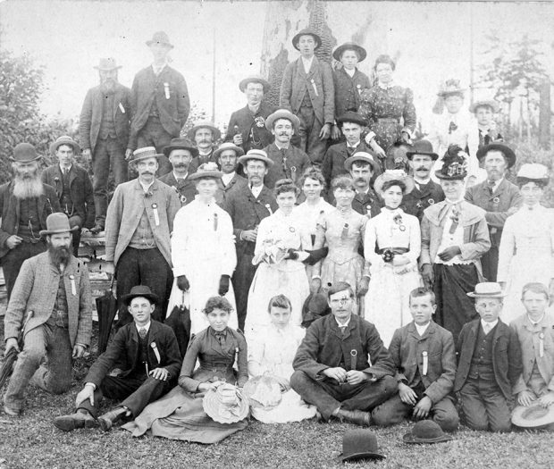 A black and white group portrait photograph of six approximate rows of formally dressed men, women, and children.