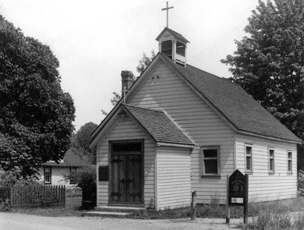 A black and white photograph of a small church building with a cross on top of the steeple.
