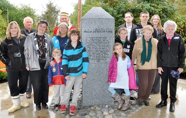 A colour photograph of men, women, and children gathered around a commemorative stone with text engraved into it. The text on the stone reads, “Philip Jackman Park.”
