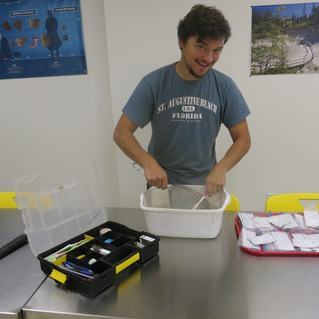 Person cleaning artifacts in a white bin with a toothbrush