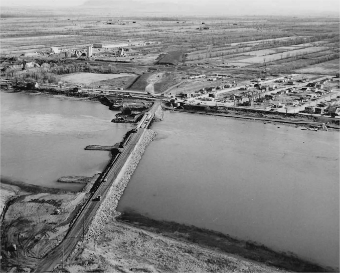 A bridge over a river with a small town and fields in the background