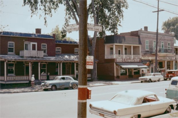 A commercial street with parked cars and pedestrians