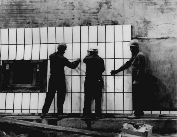 Three men installing ceramic tiling on the wall of a tunnel
