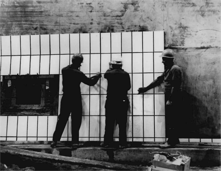 Three men installing ceramic tiling on the wall of a tunnel