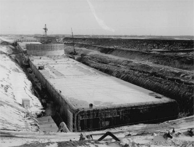 A concrete structure under construction in a trench with a crane