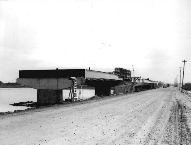 Steel girders installed on the pillars of a bridge with trucks in the background