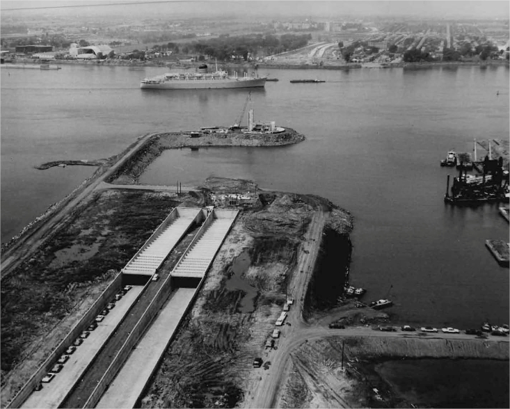 A highway under construction near a river with a boat and a city in the background