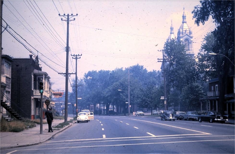 A street scene with cars and a man waiting for a bus