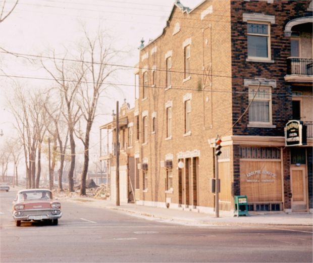 Buildings being torn down on a quiet street with a car in the foreground
