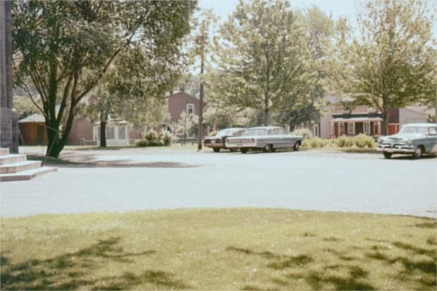 Cars parked with a park and houses in the background