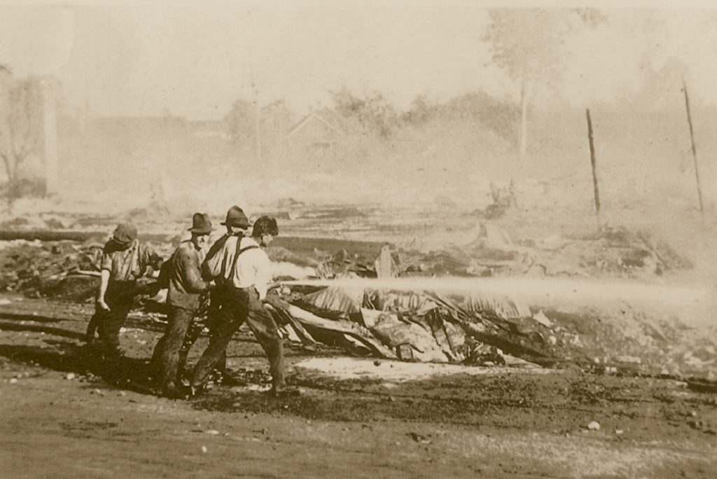 Quatre hommes, entourés par les décombres, dirigent un tuyaux d’incendie.