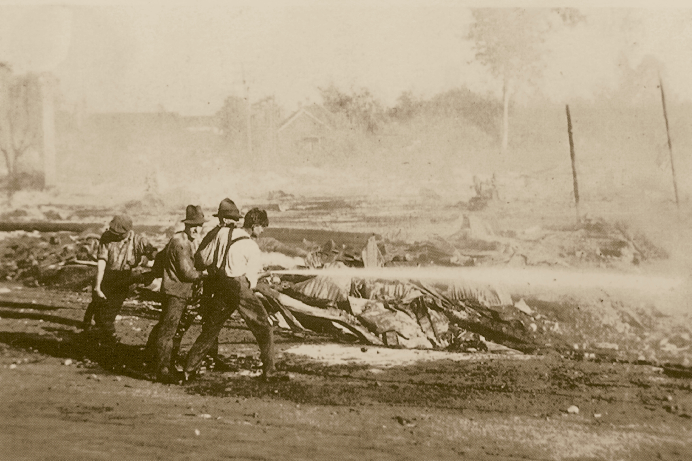 Four men surrounded by rubble directing a fire hose