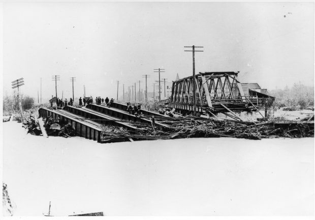 A small crowd view the remains of two washed out bridges