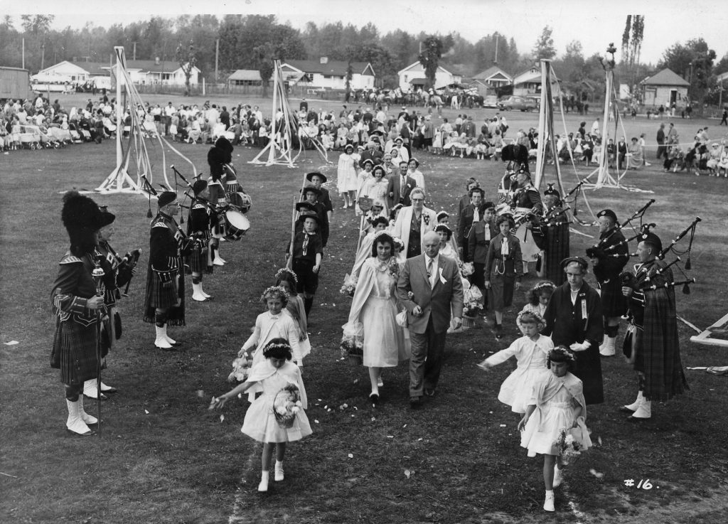 A procession of adults and children walking towards the camera across a field