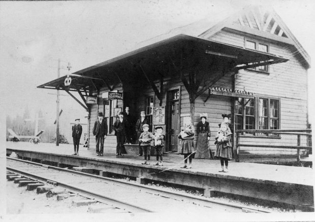 A group of adults and children pose on a train station platform