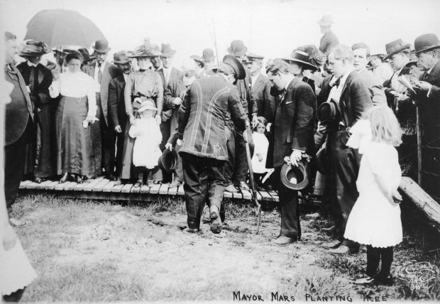 Two men standing with a shovel surrounded by onlooking adults and children