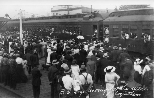 Soldiers in train cars wave to a large crowd gathered on the station platform