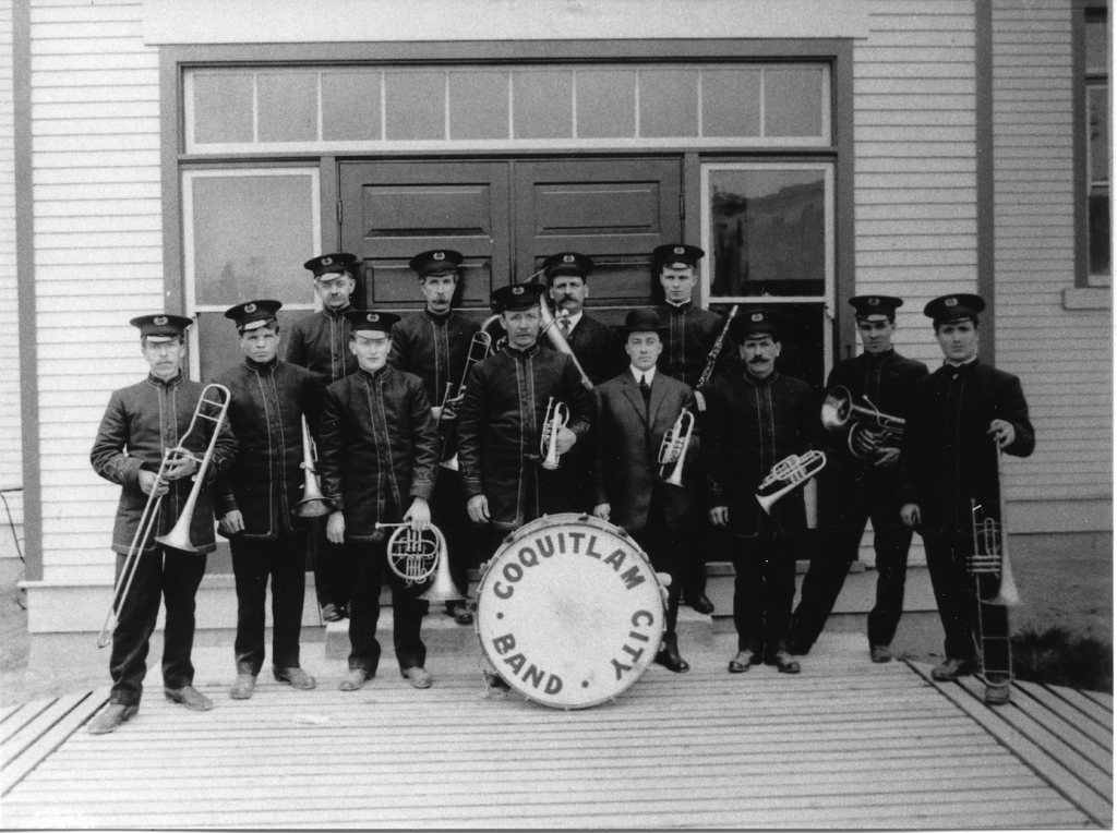 Twelve uniformed men holding various instruments pose facing the camera