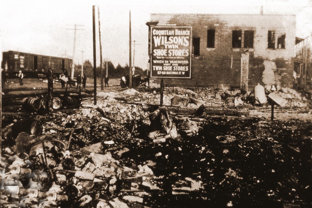 Ruins of a burnt building with a damaged stone structure in the background