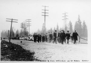 A long line of adults and children walk down a dirt road in celebration