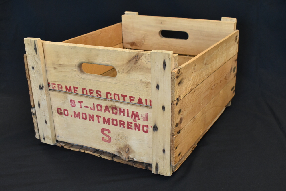 Colour photo of a wooden crate with the name “Ferme des coteaux St-Joachim Co. Montmorency S” stamped on the end facing the camera.