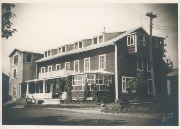 Black and white archival photo showing a three-storey, gable-roofed hotel. The main façade boasts a balcony and a veranda, and there is a solarium on the ground floor.