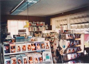 Photographie couleur montrant des étalages dans un magasin. On y voit des emballages de soutien-gorge et d’autres sous-vêtements sur des présentoirs de plancher et dans des étagères murales. Deux fenêtres laissent entrer la lumière de l’extérieur.