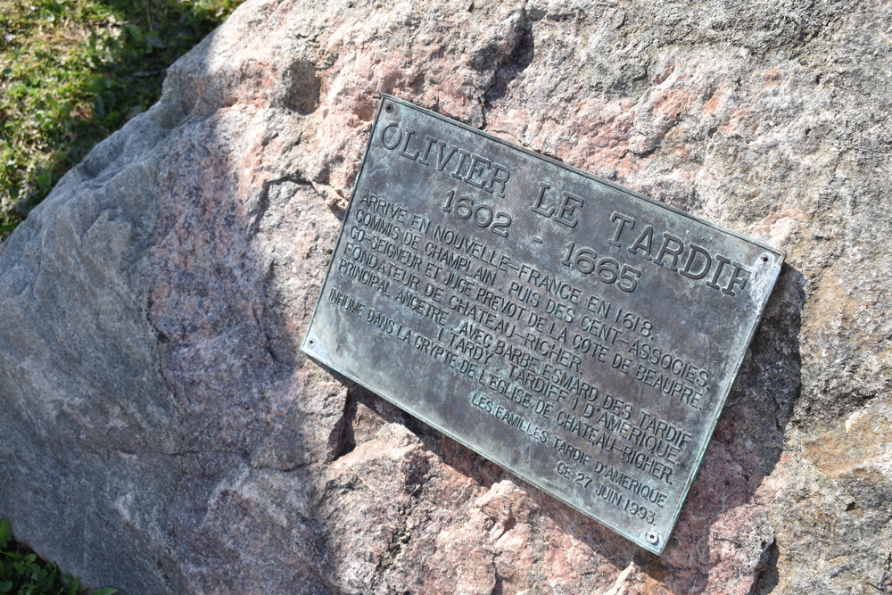 Colour photograph of a commemorative bronze plaque set into a rock that reads (translation): Olivier Le Tardif 1602-1665. Arrived in New France in 1618. Clerk of Champlain, then of Compagnie des Cent-Associés. Co-seigneur and provost-judge of Côte de Beaupré. Founder of Château-Richer. Primary ancestor, together with Barbe Esmard, of the Tardif (Tardy, Tardiff) family of North America. Interred in the crypt of the Château-Richer Church. The Tardif families of North America, June 27, 1993.