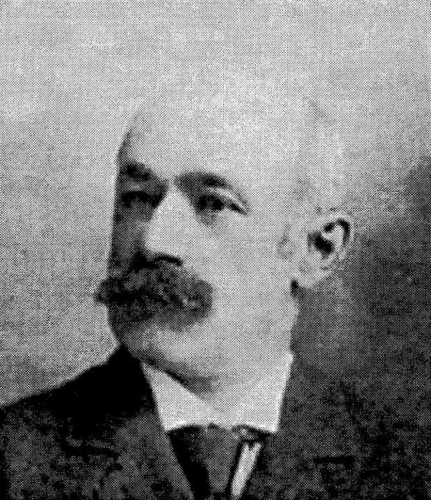 Black and white, three-quarter-view, archival portrait photo of a moustachioed Arthur Toussaint wearing a suit and tie.