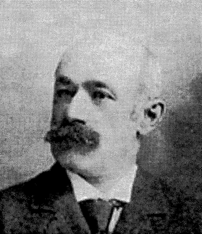 Black and white, three-quarter-view, archival portrait photo of a moustachioed Arthur Toussaint wearing a suit and tie.