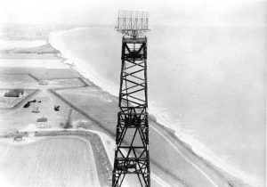 A black and white image of a radar tower with view of countryside and ocean.