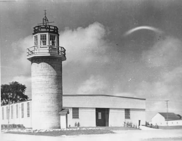 Black and white image of a guard tower/silo next to a low building.