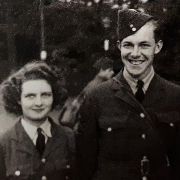 Black and white photo of a young couple in WWII Air Force uniforms, smiling at the camera.