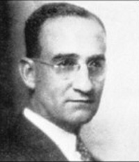 A grainy black and white portrait of a white man with glasses and slicked-back hair.